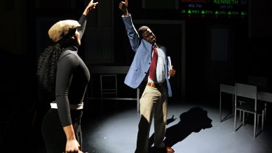 A woman holding a briefcase and a man in a suit both point upwards on a dimly lit stage, with electronic share ticker numbers displayed in the background.